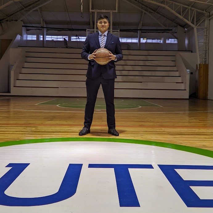 Carlos Darío Mena Baquero, de traje con un balón de baloncesto en la cancha
